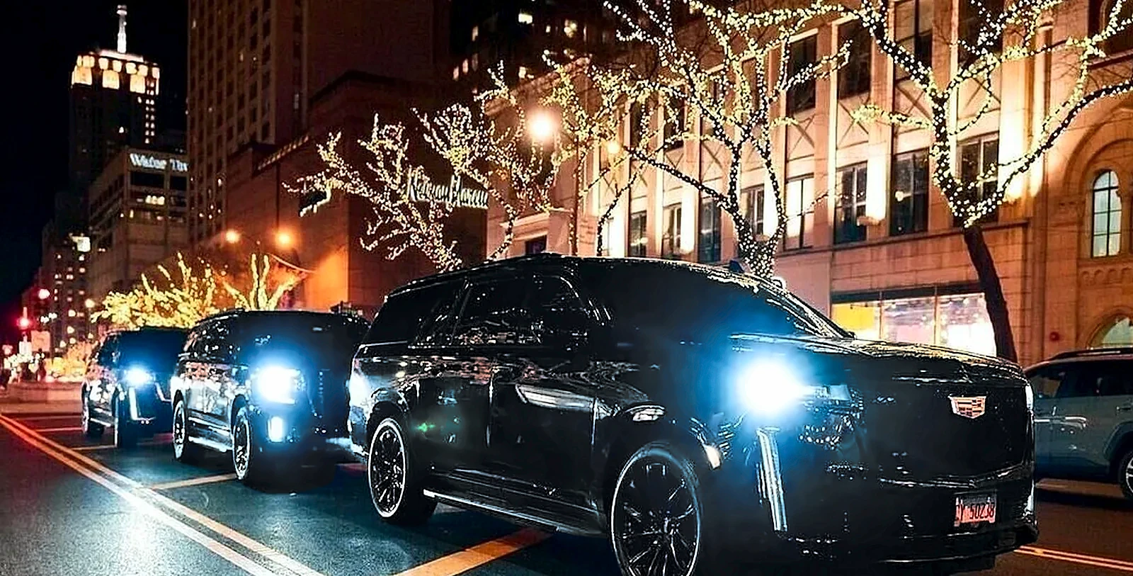Black Cadillac Escalades on Michigan Avenue under holiday lights at night